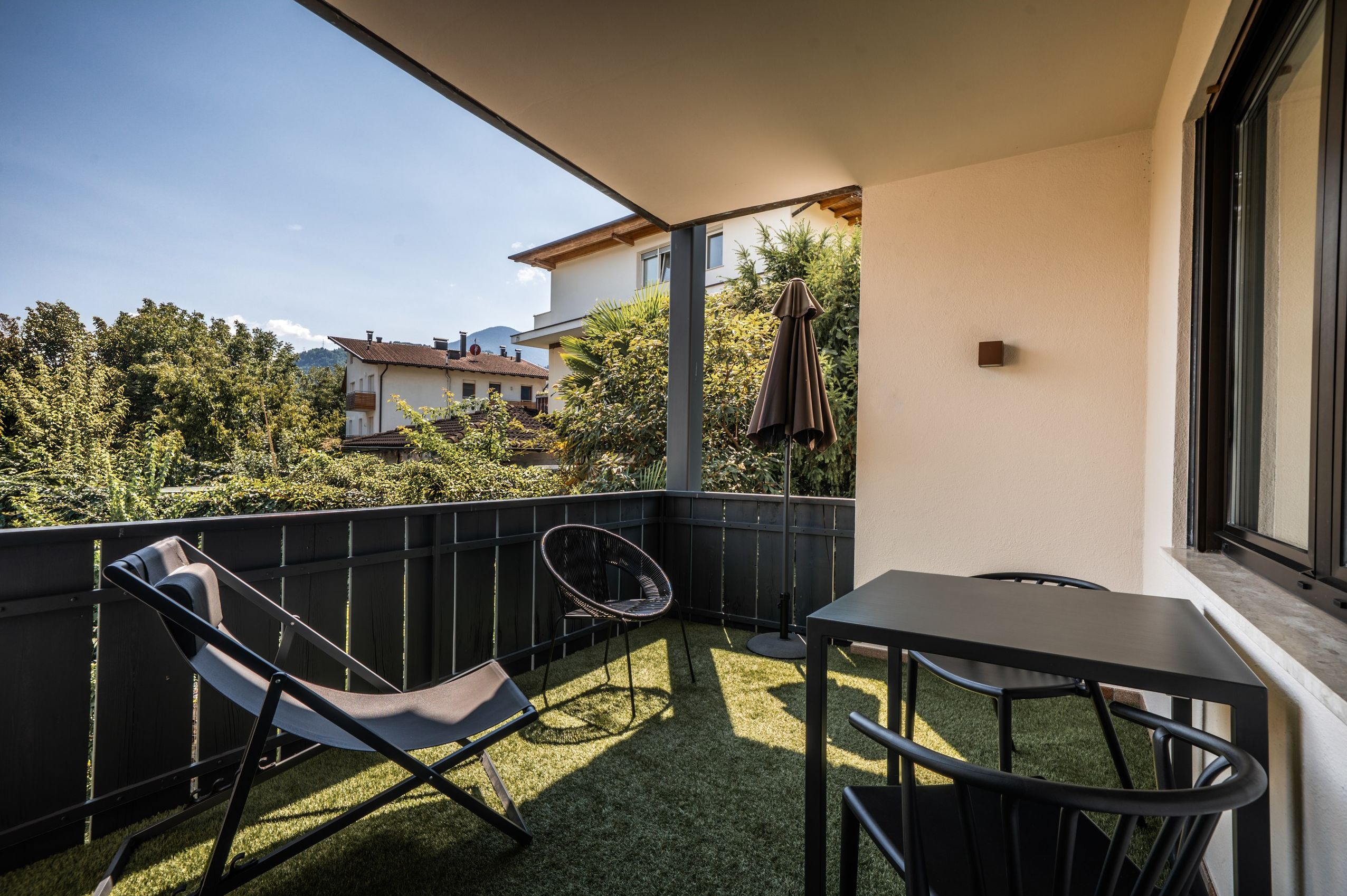 Ein Balkon mit Tisch und zwei Stühlen, Blick auf die Umgebung und eine Tür zum Innenbereich.