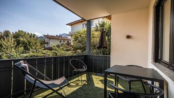 Un balcone con un tavolo e due sedie, vista sul paesaggio circostante e una porta che dà all'interno.