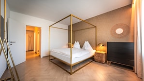 Quarto moderno com cama de dossel, piso de madeira, cômoda escura e luminária circular fixada na parede.
