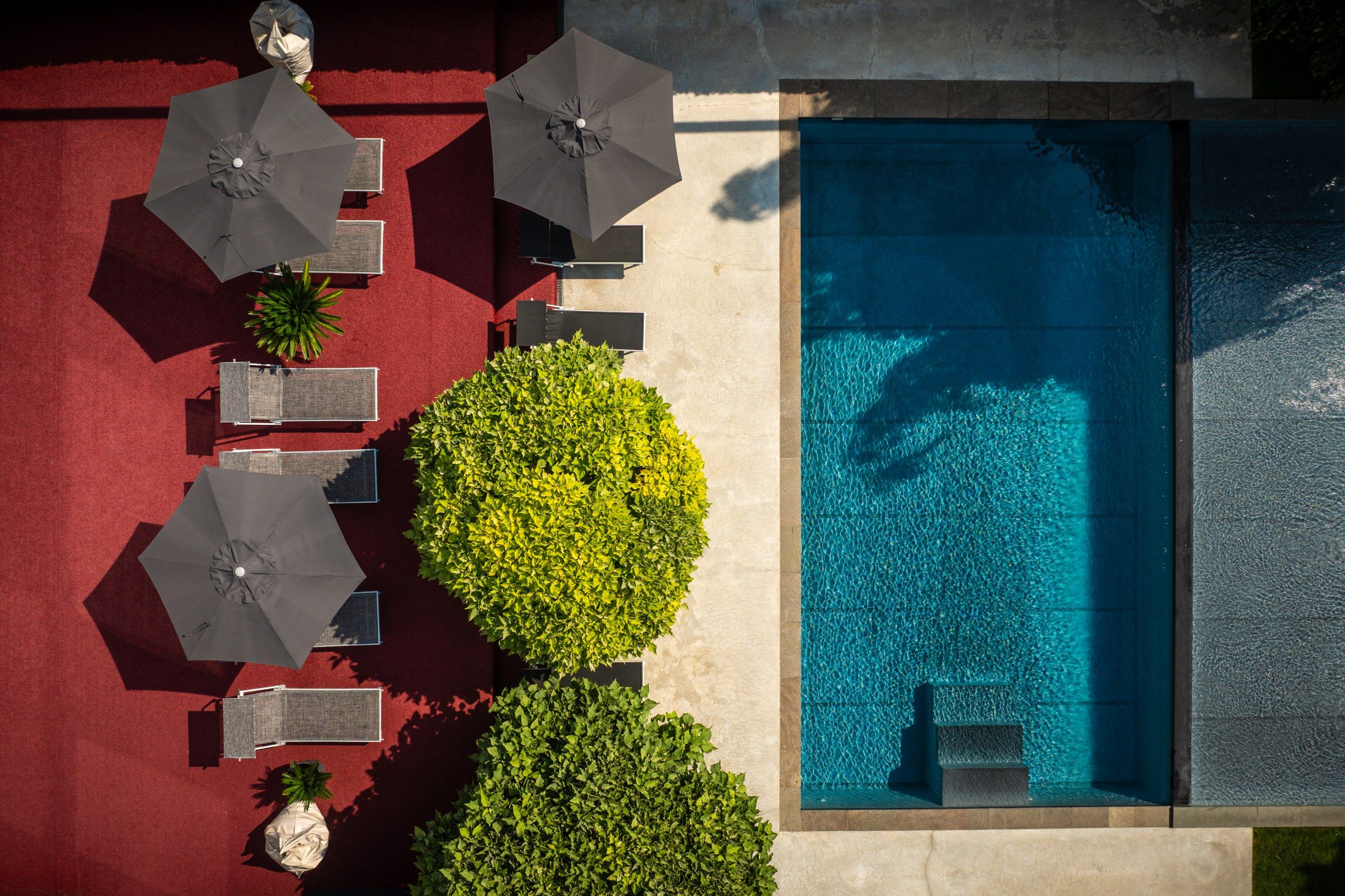 Eine Vogelperspektive eines Poolbereichs mit mehreren Sonnenschirmen, Sitzgelegenheiten und einem klaren, blauen Pool.