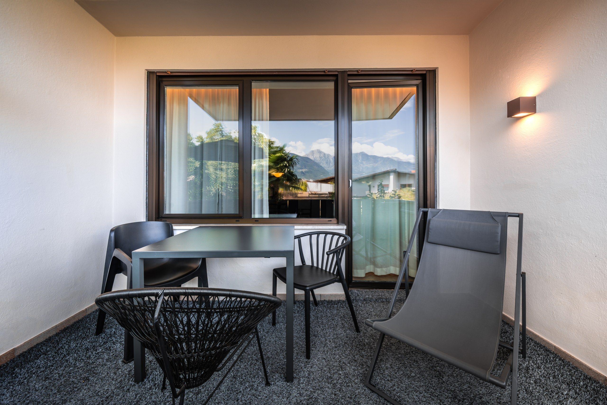 Ein Zimmer mit Tisch und Stühlen, Blick auf Berge und einem Balkon mit einem Stuhl.