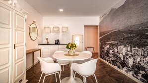 A modern room with a dining table, white chairs, a kitchen area, and a mural on the wall. - 739D goldfinger+suites I Apartment Individual 12 (Lana)