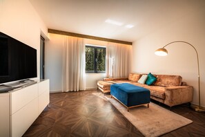 A modern living room with a flat-screen TV, a sofa, a coffee table, and a floor lamp. - 739D goldfinger+suites I Apartment Individual 12 (Lana)