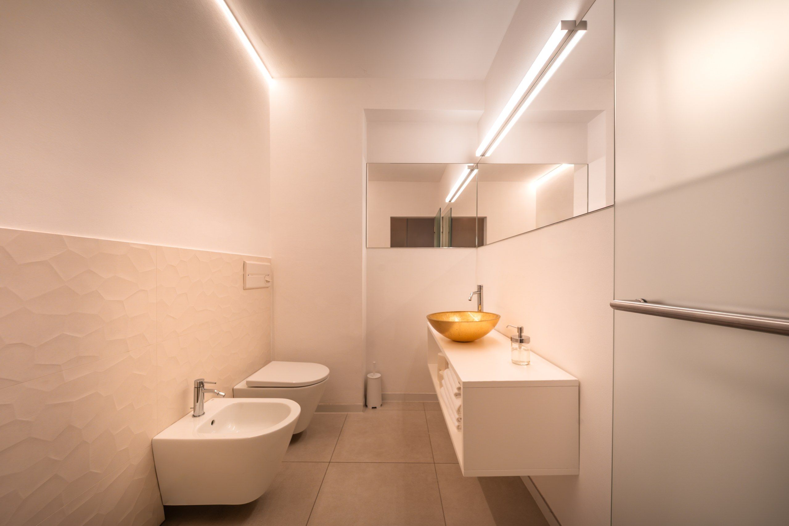 Een moderne badkamer met een toilet, een wastafel met een grote waskom en een bidet.