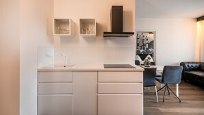 Cocina moderna con armarios blancos, campana extractora negra y comedor con sofá de cuero negro y dos sillas.