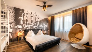 Een moderne slaapkamer met een groot bed, een opvallende stoel in de vorm van een ei, een plafondventilator en een muurschildering.