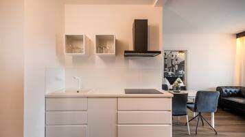A modern kitchen with white cabinetry, a black range hood, and a dining area with a black leather sofa and two chairs.