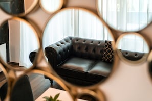 En moderne stue med en mørk lædersofa, et sofabord og et stort spejl der reflekterer rummet.