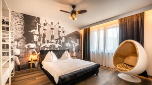 Un dormitorio moderno con una cama grande, una silla de diseño con forma de huevo, un mural en la pared y vistas a la ciudad a través de la ventana.