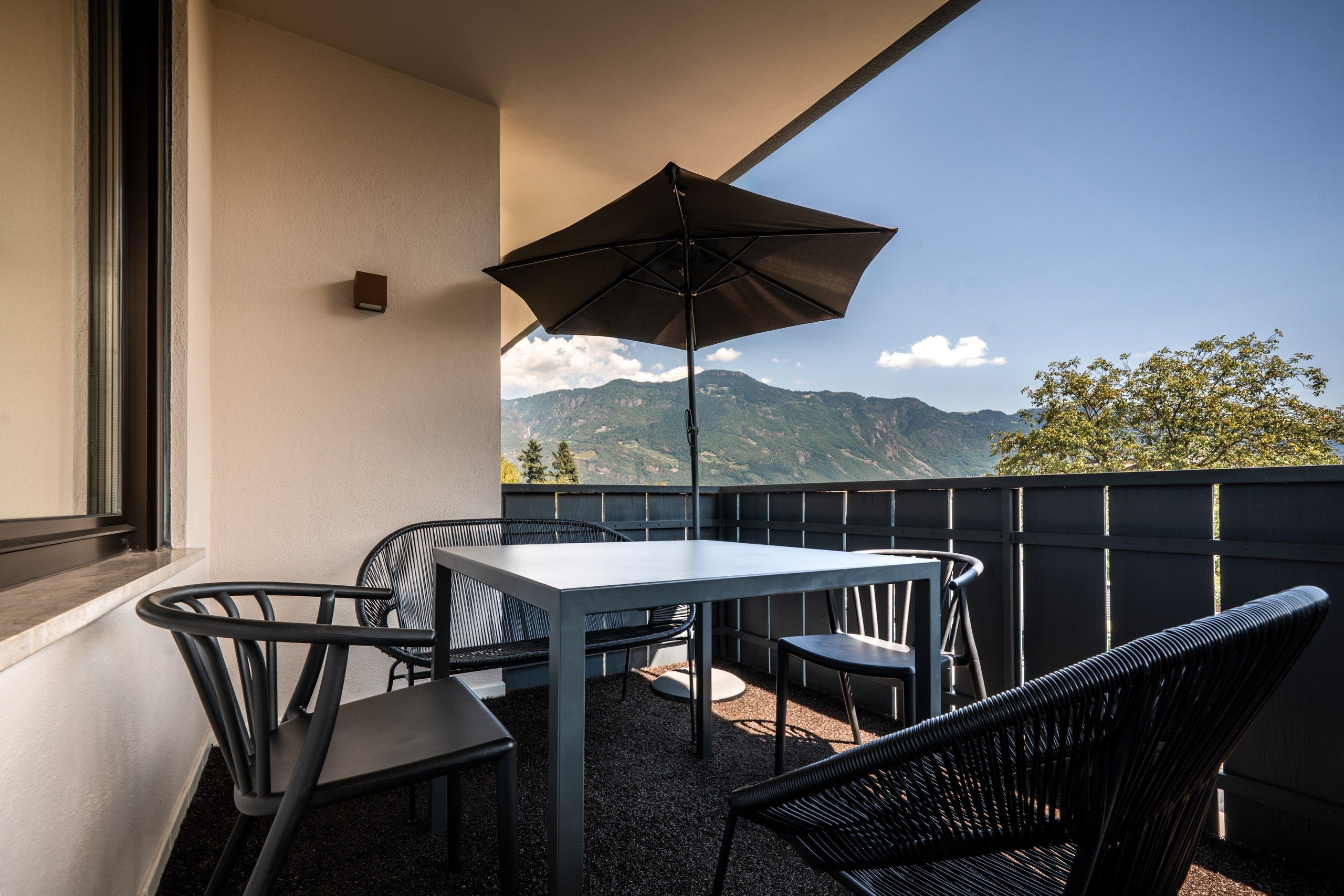 Een balkon met een tafel, stoelen, een grote parasol en uitzicht op een berg.