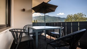 Een balkon met een tafel en stoelen, een grote parasol en uitzicht op een berg.