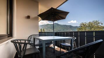 A balcony with a table and chairs, a large umbrella, and a mountain view.