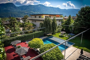 Ein modernes Hotel mit Schwimmbad, umgeben von üppiger Vegetation und Bergen im Hintergrund.