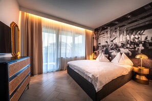 A modern hotel room with a large bed, a dresser, a large window with sheer curtains, and a wall-mounted painting. - 739G goldfinger+suites I Apartment Extraordinary 1 (Lana)