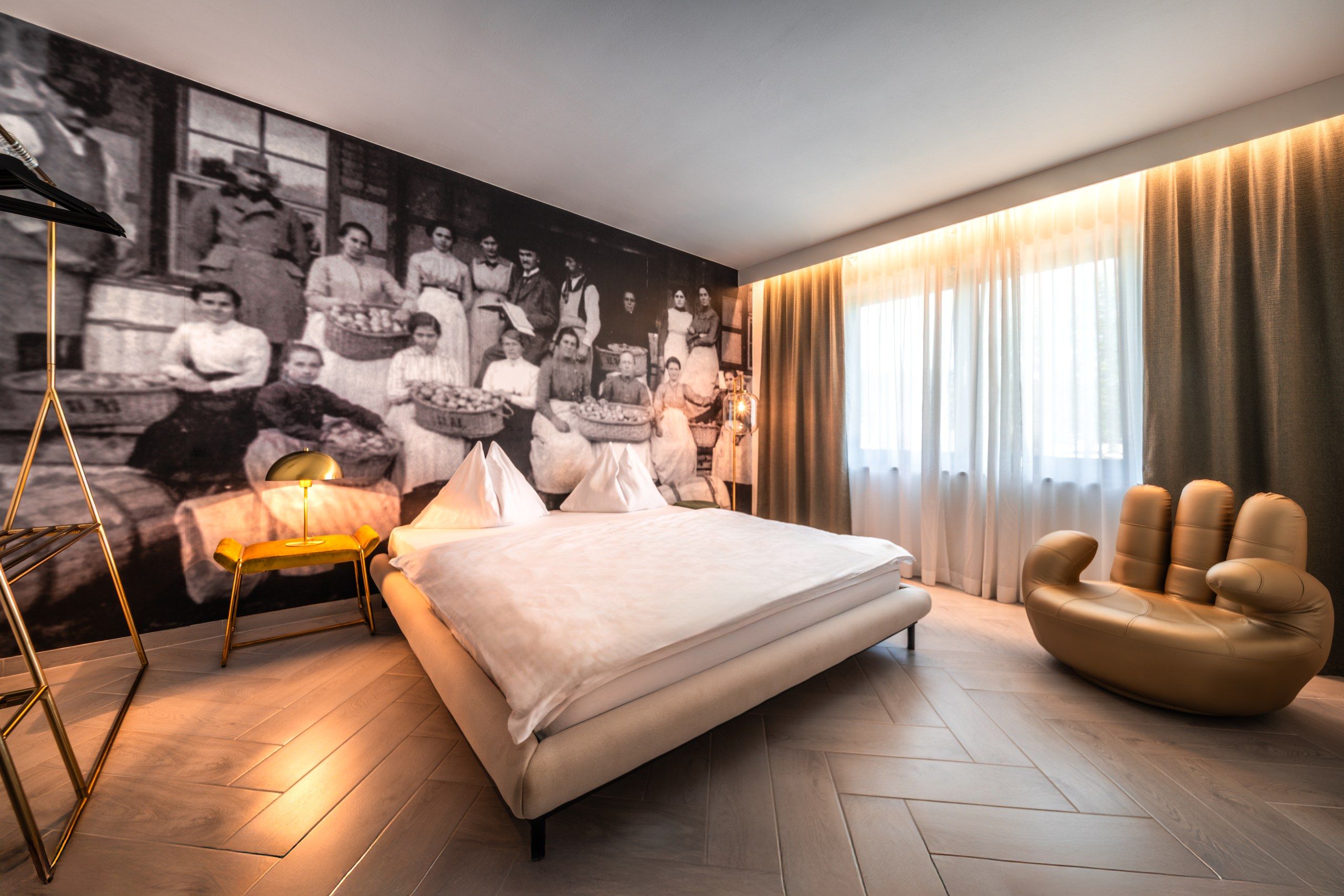 Een moderne slaapkamer met een groot bed, een bijzondere stoel, een vloerlamp en een muurschildering.