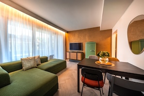 Ein modernes Wohnzimmer mit einem grünen Sofa, einem Esstisch mit Stühlen, einem Flachbildfernseher und einer grünen Kommode.
