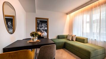 A modern living room with a green sofa, a dining table with chairs, and a mirror on the wall.
