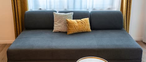 A sofa with two cushions, a small round table, and a mirror on the floor.