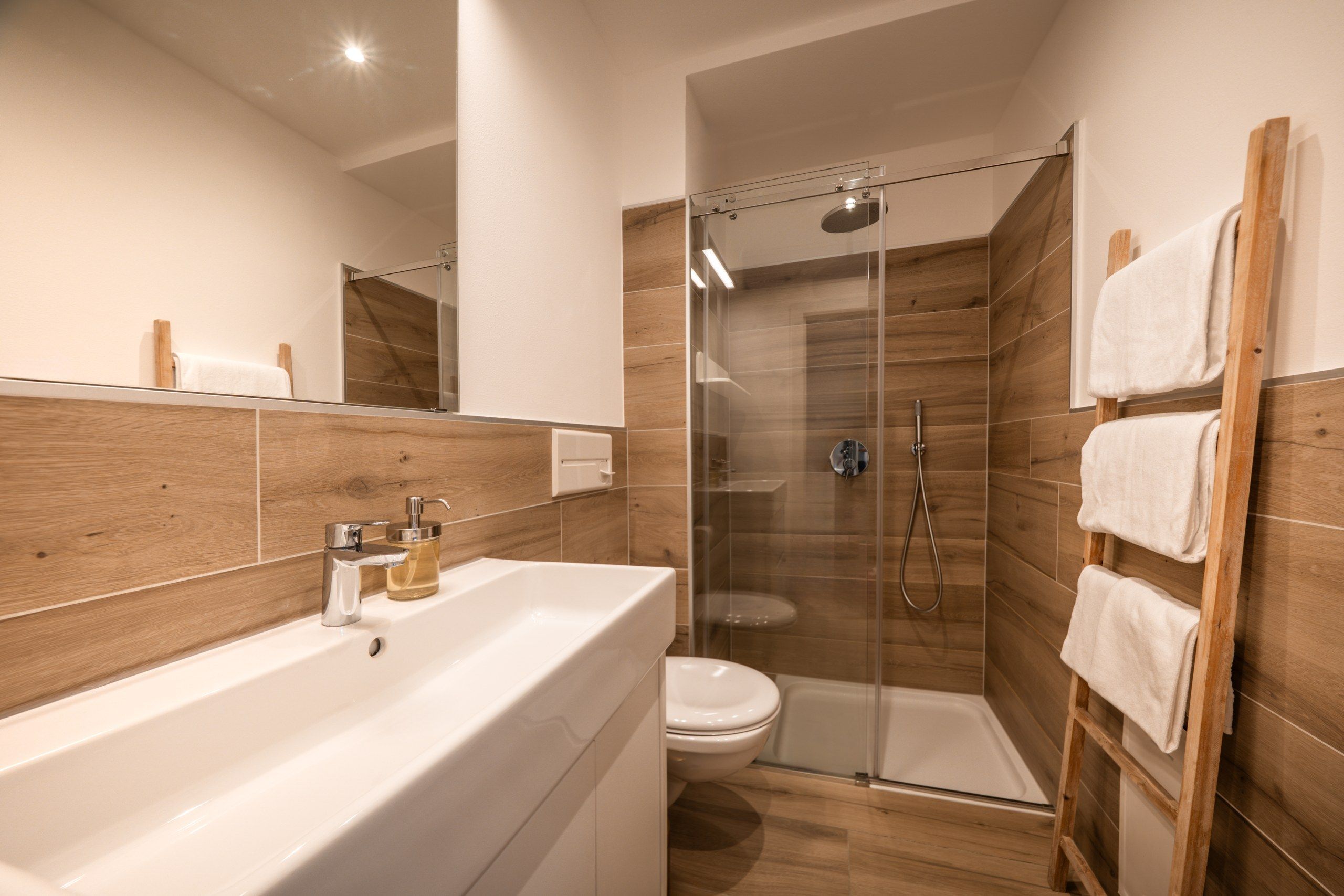 A modern bathroom with a glass-enclosed shower, a white sink, and wooden paneling.