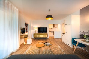 A modern living room with a flat-screen TV, a sofa, a coffee table, and a dining area with a table and chairs. - 739L Goldfinger+Suites I Apartment Unique 24 (Lana)