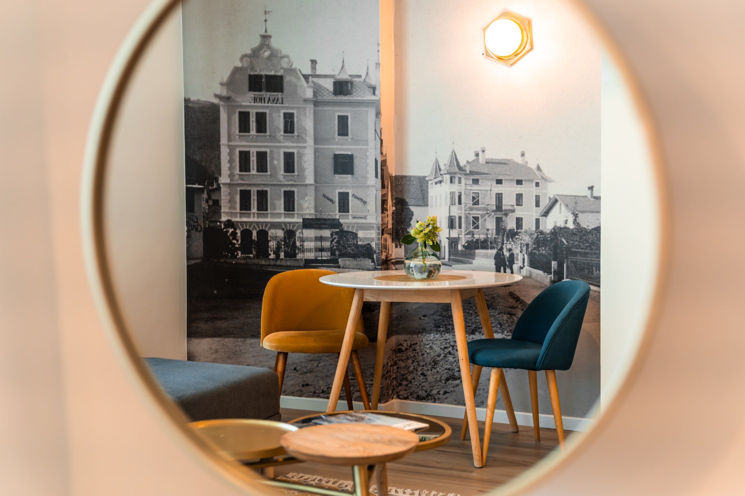 A room with a round table, two chairs, a vase with flowers, and a large framed photograph of buildings.