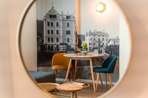 Una habitación con una mesa redonda, dos sillas, un florero con flores y una fotografía grande enmarco de edificios.