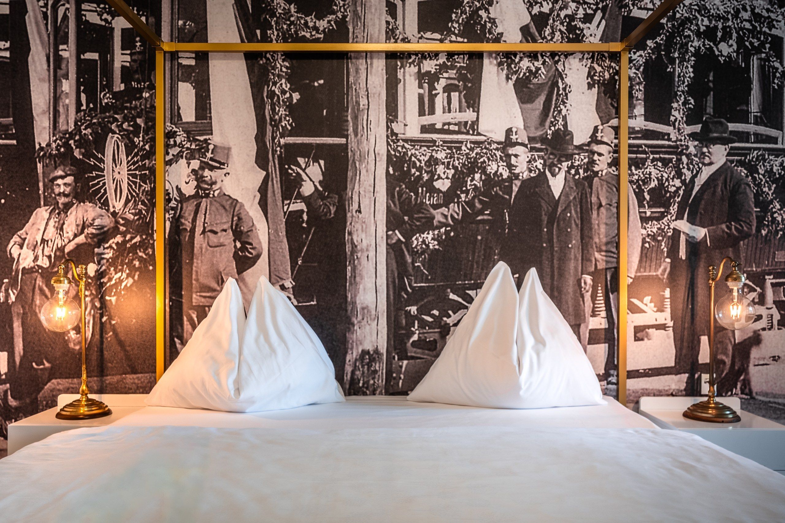 Een bed met twee witte kussens en een zwart-wit historisch foto op de achtergrond.