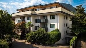 A modern two-story building with a flat roof, multiple balconies, and a surrounding garden.