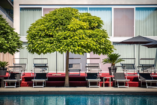 Zona junto a la piscina con sillones de descanso y un árbol.