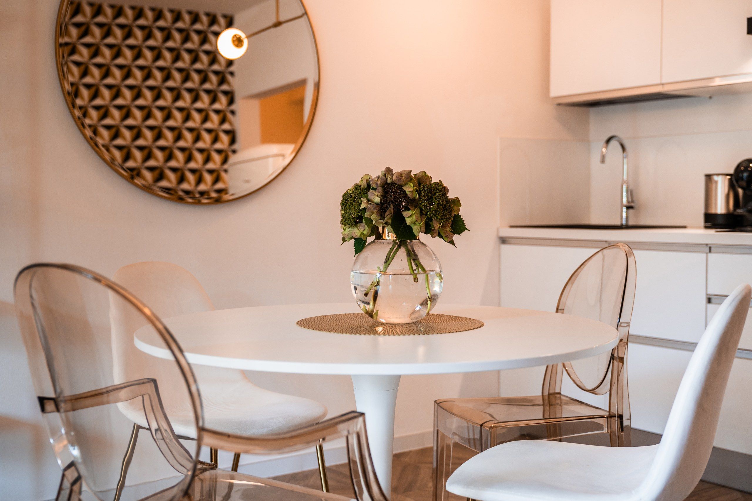 A modern kitchen with white cabinets, a round dining table with chairs, and a decorative vase with flowers.