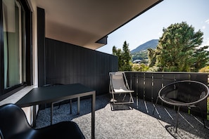 Un balcón con una mesa y sillas, vistas a árboles y montañas, y una valla de madera.