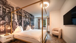 A four-poster bed with a gold frame, a nightstand with a lamp, and a wall with a large black-and-white photograph.