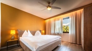 Ein Hotelzimmer mit einem Bett, zwei Nachttischlampen, einem Deckenventilator und einem Fenster mit Vorhängen.