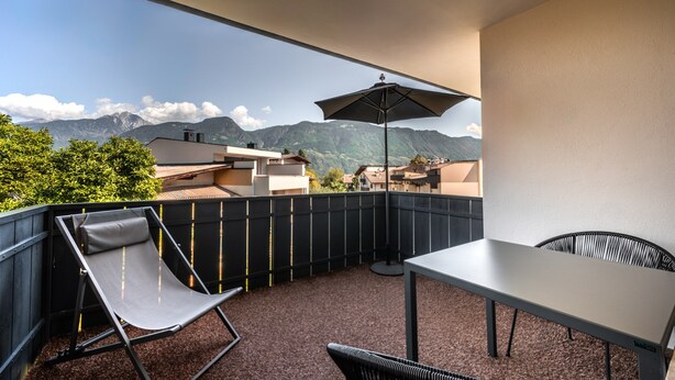 Ein Balkon mit Tisch, zwei Stühlen und Sonnenschirm.