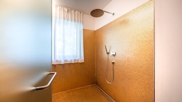 Een douche met een structuurwand, een raam met een wit gordijn en een douchekop.