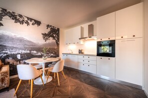 A modern kitchen with white cabinetry, a built-in oven, and a dining area with a round table and chairs.