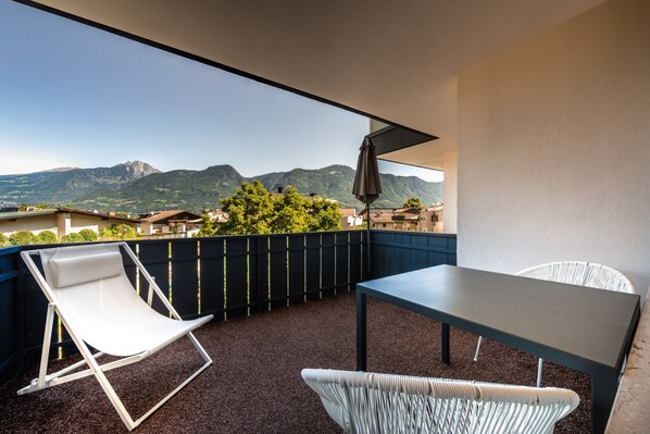A balcony with a table and chairs, a view of mountains, and a clear sky.