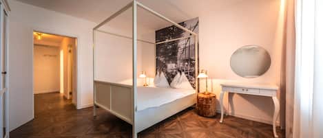 A four-poster bed with a night sky mural, a bedside table with a lamp, and a round mirror on a white dresser.