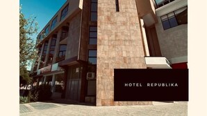 A modern hotel building with a prominent central tower, multiple windows, and a paved entrance area. - Hotel Republika Berat (Velabisht)