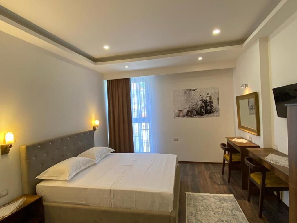 A hotel room with a large bed, bedside lamps, a desk, a chair, and a television.