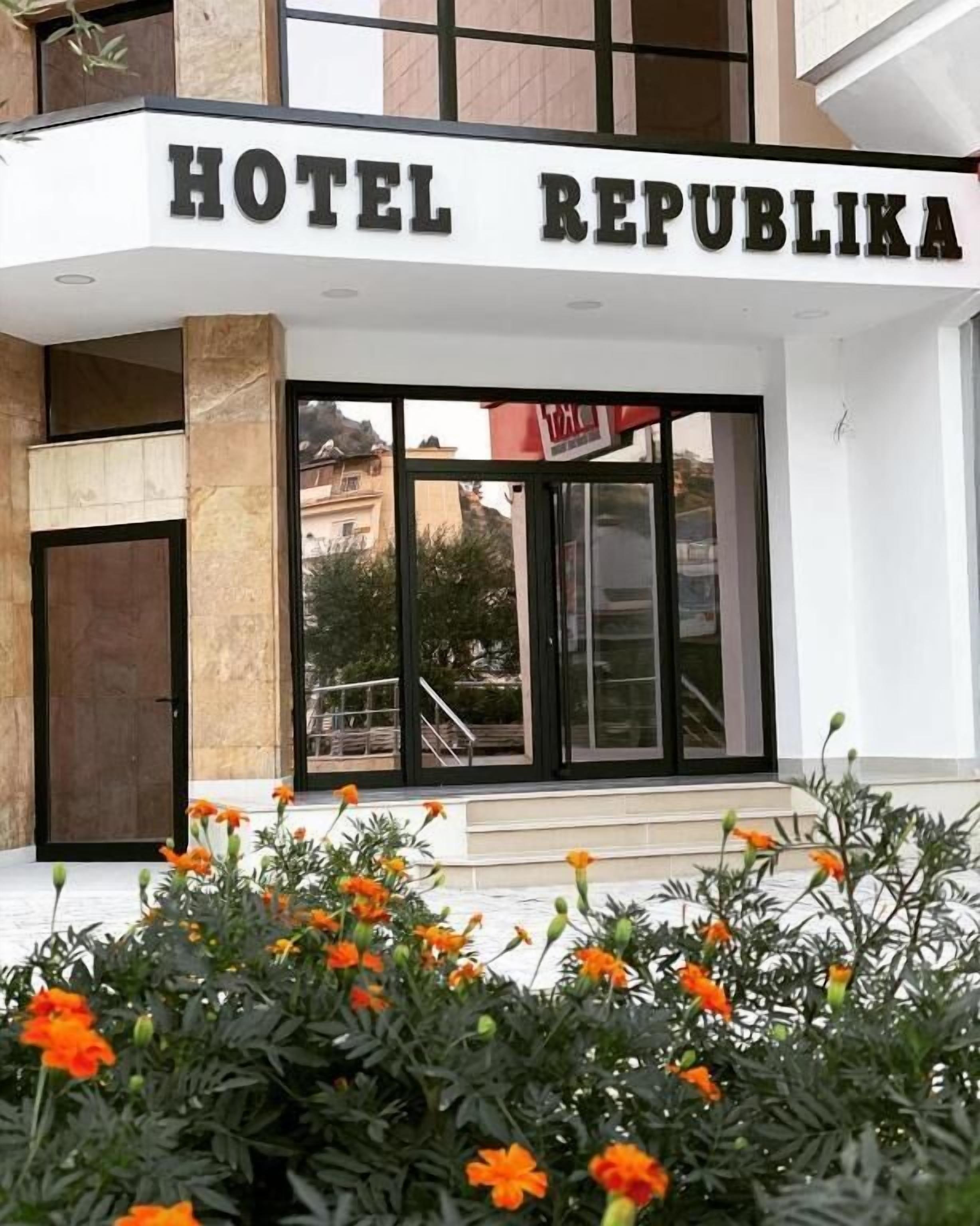 La entrada del Hotel Republikka, con un diseño moderno, presenta amplias puertas de cristal y una escalera visible que conduce a la recepción.