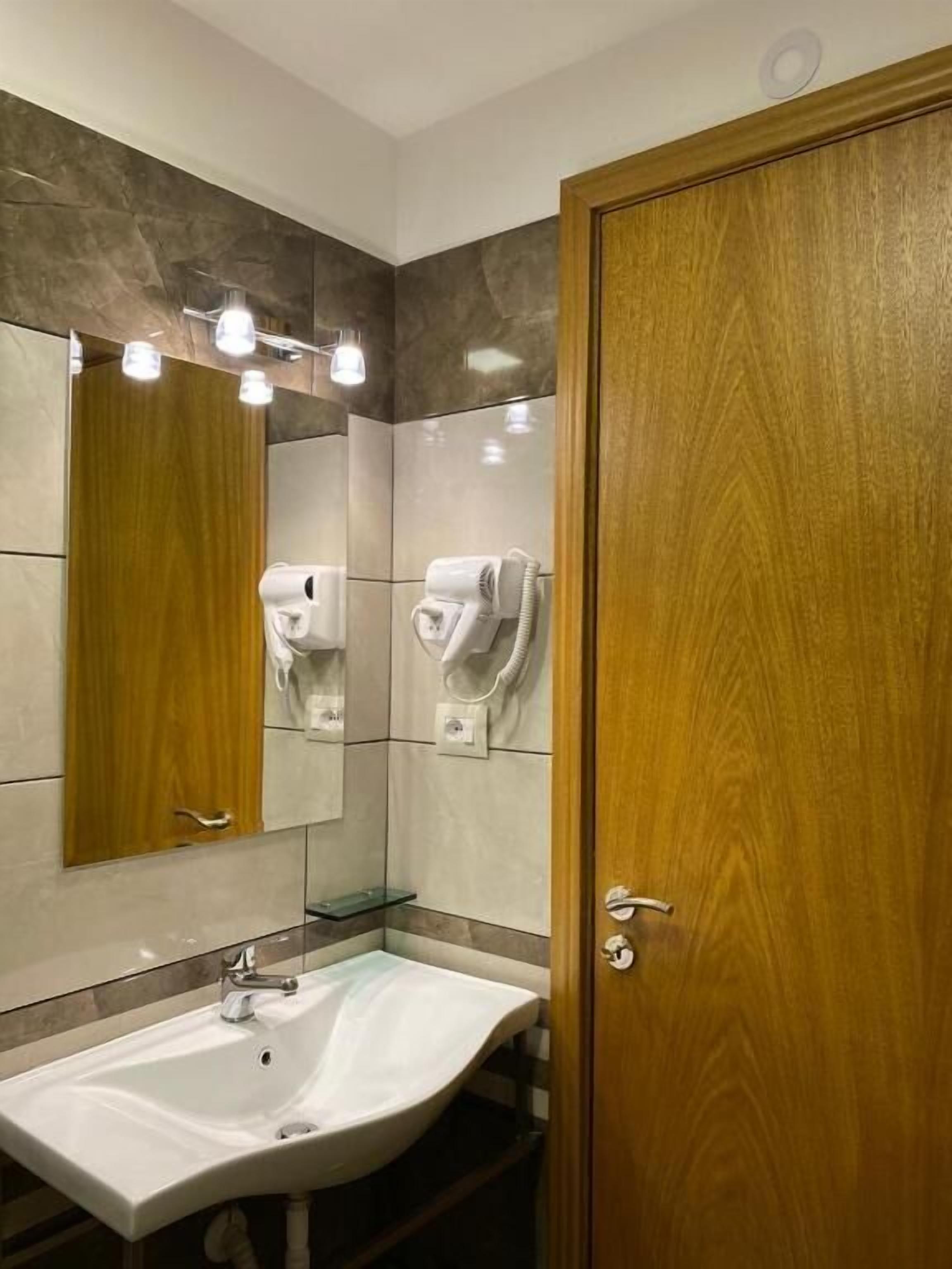 Un baño con puerta de madera, un lavamanos blanco y dos secadores de pelo montados en la pared.