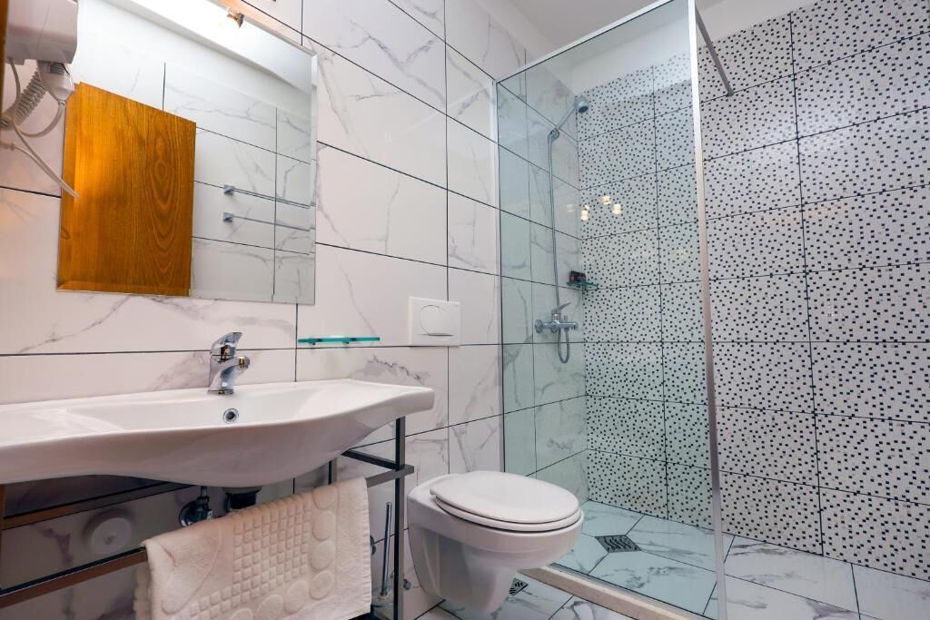 Un baño moderno con lavamanos de mármol, cabina de ducha de vidrio y un inodoro.