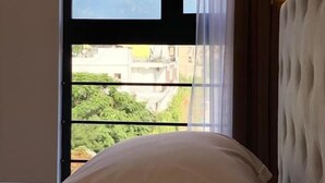 A hotel room with a bed, a window with a view of buildings and greenery, and a bedside lamp. - Hotel Republika Berat (Velabisht)