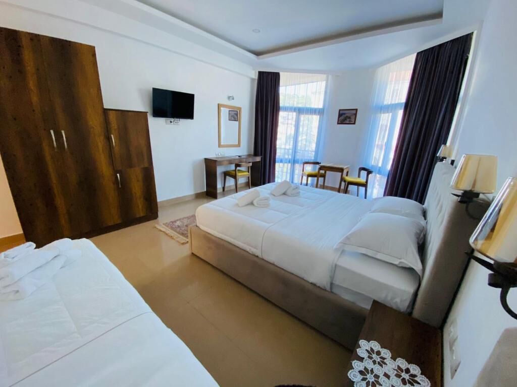 A hotel room with a bed, a desk, two chairs, a TV, and a wardrobe.