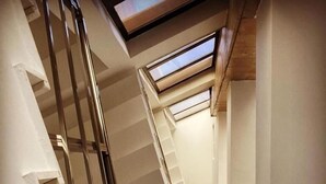 A staircase with white walls and a metal handrail, leading to a landing with a window. - Hotel Republika Berat (Velabisht)