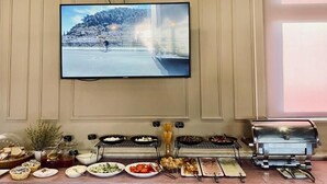 A buffet setup with various dishes, a television mounted on the wall, and a grill. - Hotel Republika Berat (Velabisht)