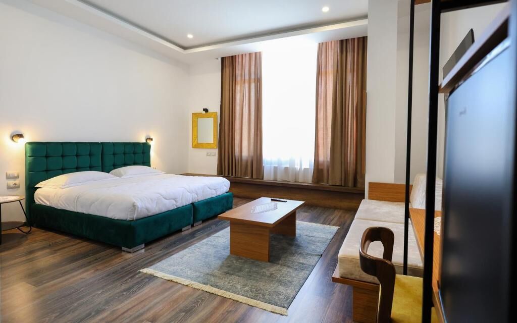 Et moderne hotelværelse med en stor seng, en lille sofa, et træbord og et stort vindue med gardiner.