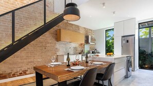 A modern kitchen with a wooden dining table, black chairs, and a staircase with a mesh railing. - Views, Fireplace, Sea Point - Mnt Nelson Townhouse (Cape Town)