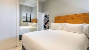 A bedroom with a large bed, a wooden headboard, and a mirror reflecting the room. - Views, Fireplace, Sea Point - Mnt Nelson Townhouse (Cape Town)